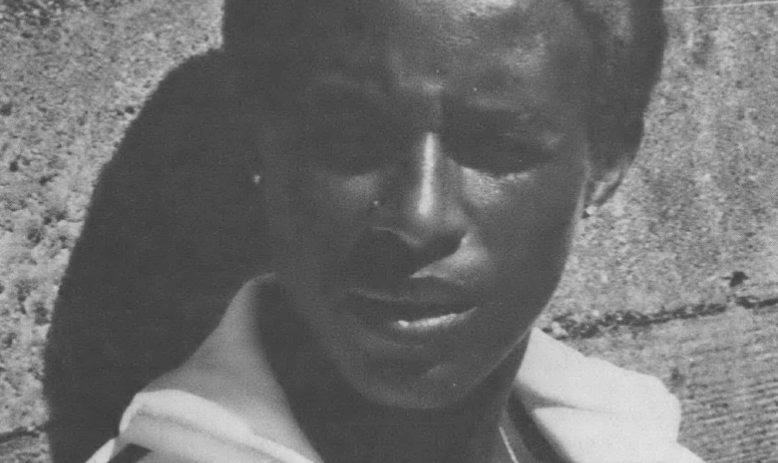 Black and white photo of Black woman with grey streaks in her hair leaning against a wall