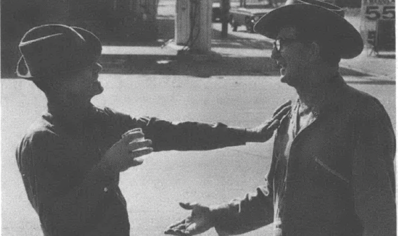 Black and white photo of two men in cowboy hats talking to each other on the street
