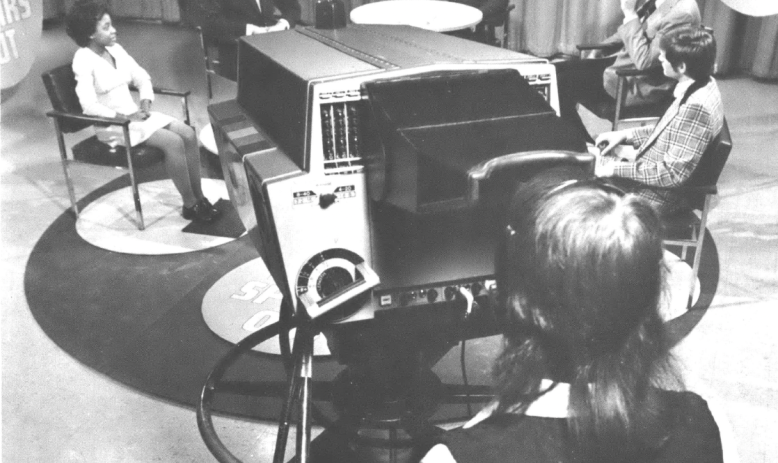 Five people sitting before a cameraman in a TV studio