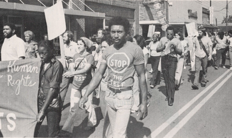 Black and white photo of people marching with banners and signs in the street
