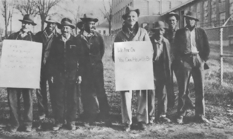 Black and white photo of group of men in bowler hats, some holding signs 