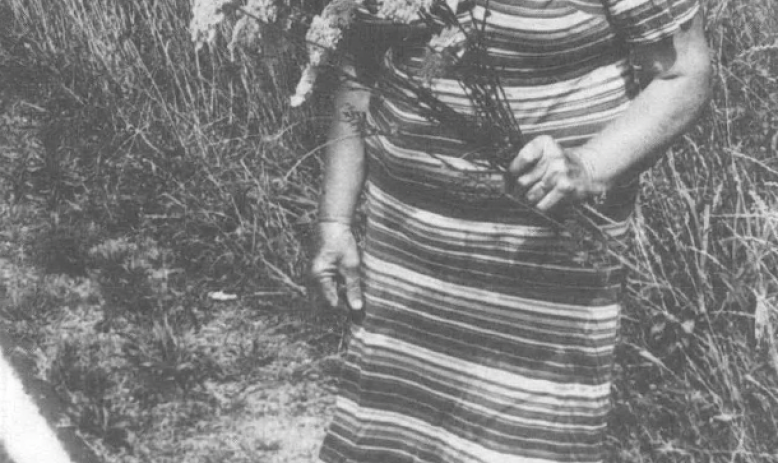 Black and white photo of woman in striped dress holding flowers and looking away from camera