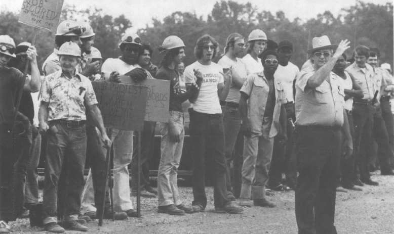 Black and white photo of group of picketers standing behind a police officer
