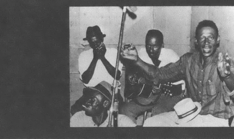 Black and white photo of four Black men seated around microphone