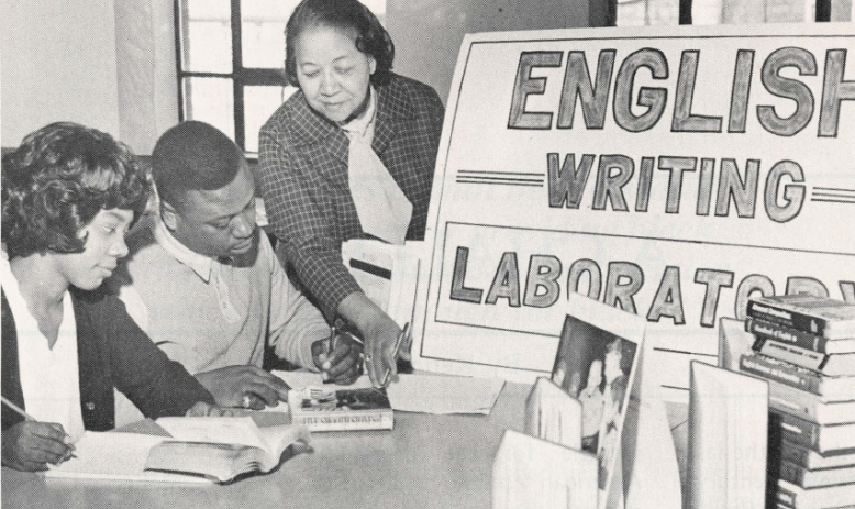 Black and white photo of Black students and teacher at a table with sign reading "English writing laboratory"