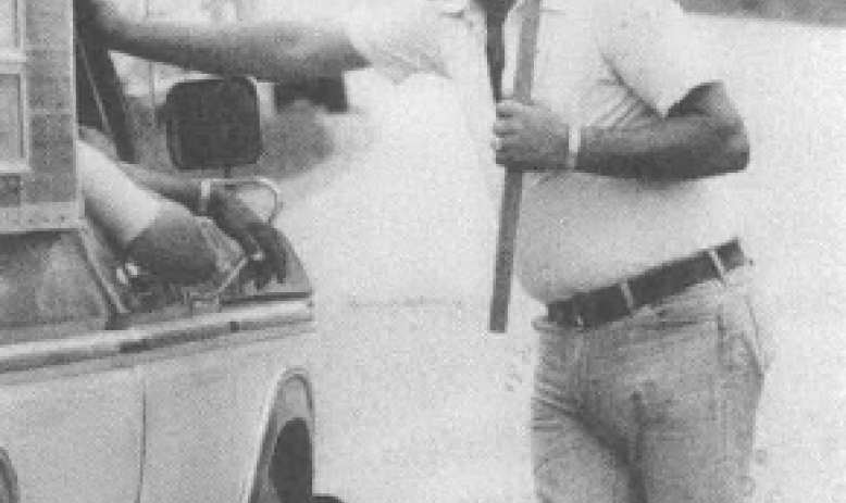 Photo of man in hard hat on picket line holding sign talking to someone in a pickup truck