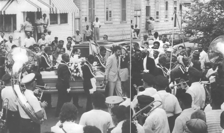 Photo of people leading hearse through street full of mourners