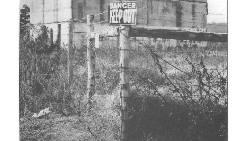 Black and white photo of fence with "keep out" sign