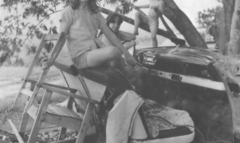 Black and white photo of white child sitting on a wooden playset outside