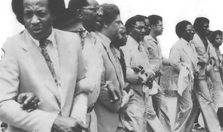 Black and white photo of Black men in suits standing arms locked in a line