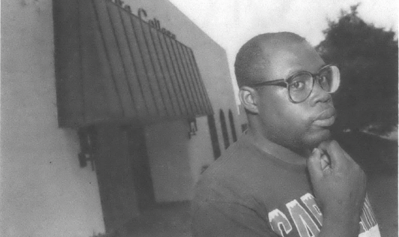 Black man with glasses and hand on chin posing in front of office building