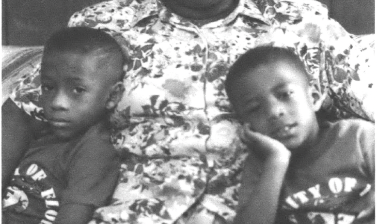 Black woman in floral dress seated holding two young children
