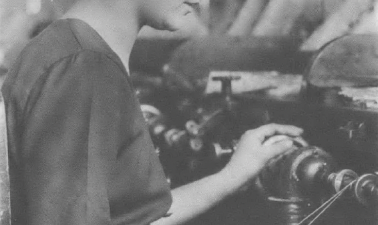 Black and white photo of woman standing at machine