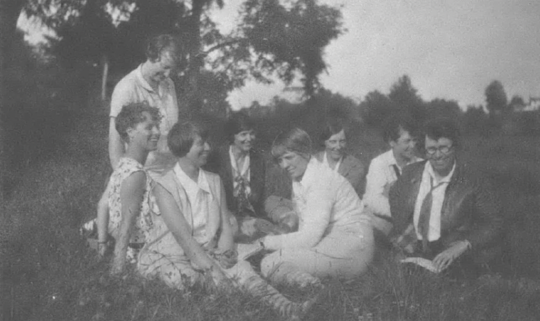 Black and white photo of group of women sitting in a circle outside