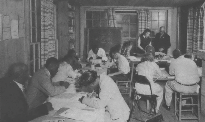 Black and white photo of people in a small schoolhouse room studying 