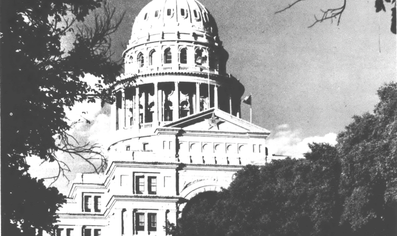 Black and white photo of the Texas State Capitol seen through trees.