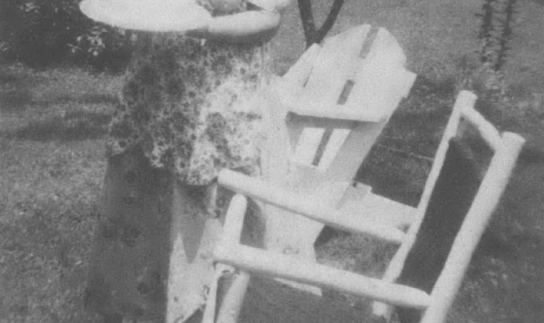 Black and white photo of elderly white woman standing outside next to rocking chairs