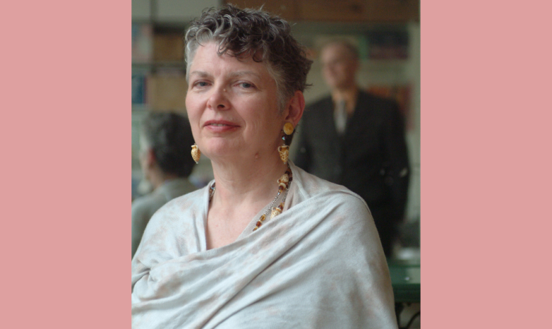 A portrait of a woman with short grey hair smiling softly at the camera, against a soft pink background