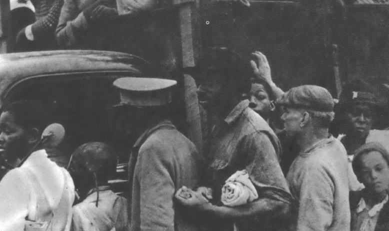 Black and white migrants crowding around a truck full of migrants