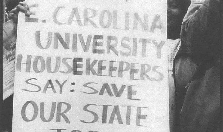 Woman holding sign that says "E Carolina Universty Housekeepers Say: Save Our State Jobs"