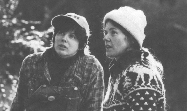 Black and white picture of two women in hats, one in overalls and one in a sweater