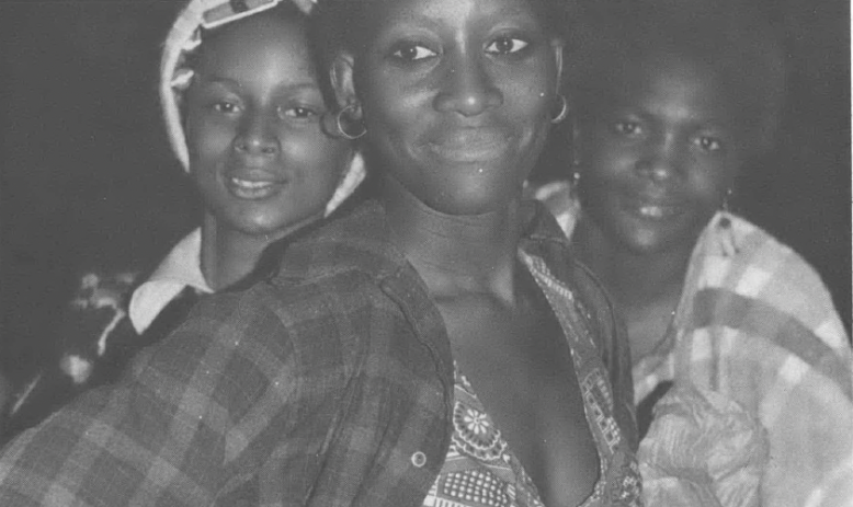 Black and white photo of three young Black women smiling at camera