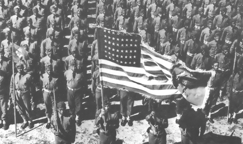 Black and white photo of rows of soldiers with an American flag in front