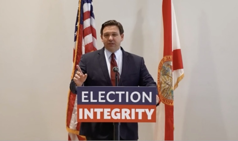 Florida Gov. Ron DeSantis speaking at a podium with a sign on it saying "election integrity"