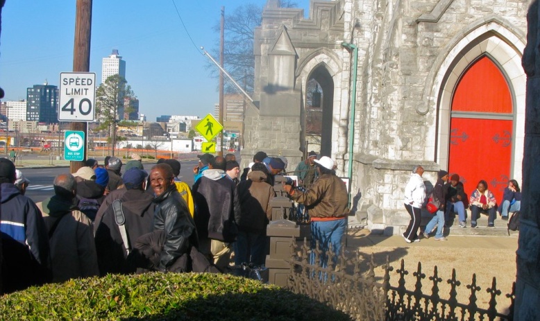 People stand in line outside a stone church with a bright red door