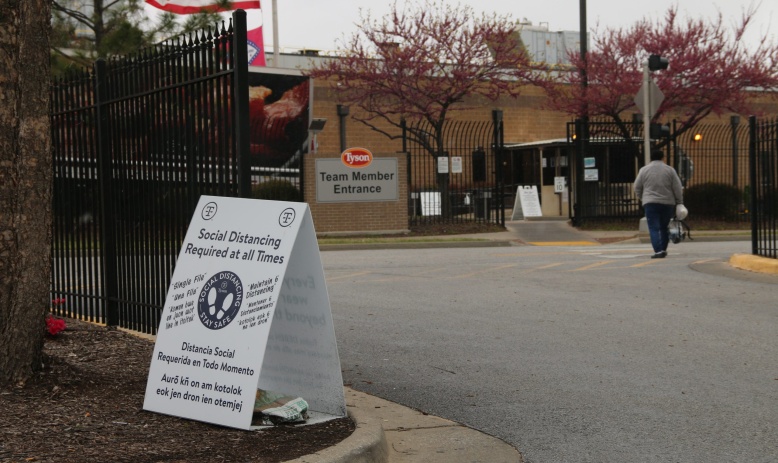 A Tyson employee walks into the team member entrance at the Berry Street location in Springdale, Arkansas. A sign in their path read "Social Distancing Required at all Times" written in English, Spanish and Marshallese.