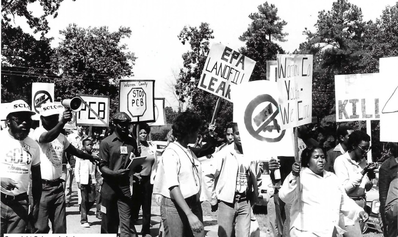 Several demonstrators, some wearing caps that read SCLC, walking and holding signs that say Stop PCB, EPA Landfill Leaks, and other slogans