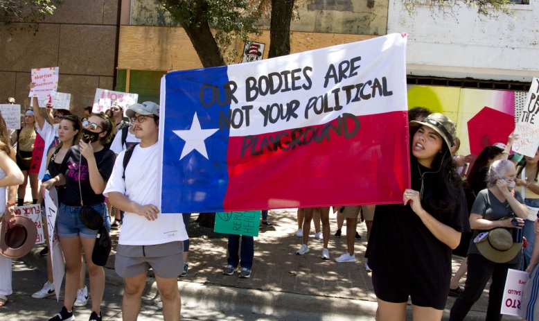A man and a woman hold a Texas flag with the text "Our Bodies Are Not Your Political Playground" written on it