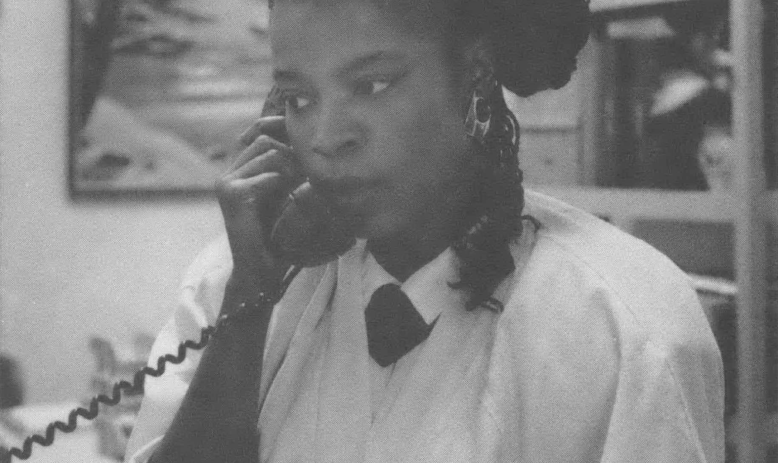 Black and white photo of a Black woman on the phone in an office. 