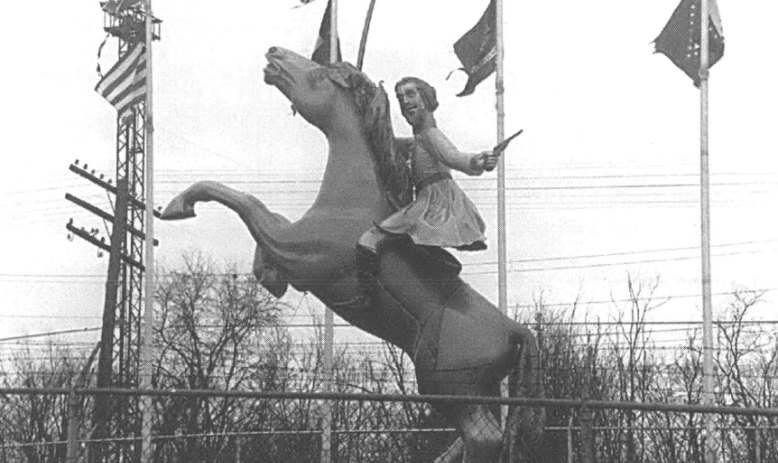 A black and white photo of a statue of a man on a horse, surrounded by several tattered flags, including Confederate flags.