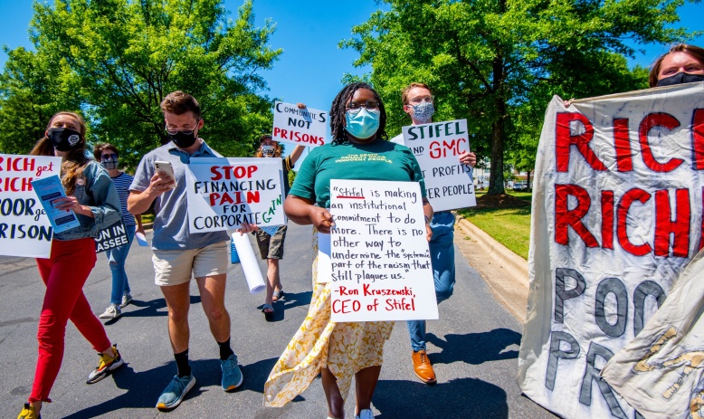 Several people walking down a street holding signs in protest of Alabama's prison lease plan