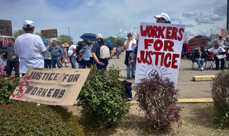 Workers mill about outside holding signs calling for justice