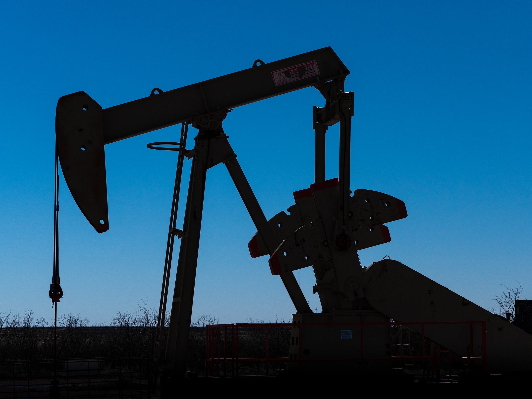 Silhouette of a pumpjack - a large metal lever-like machine - against a blue evening sky