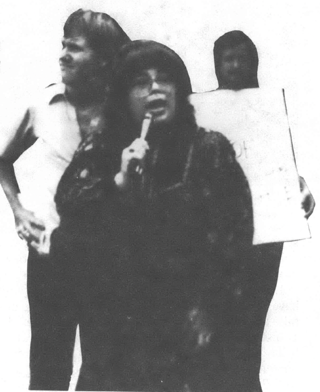 Black and white photo of three women, one of them speaking into a microphone
