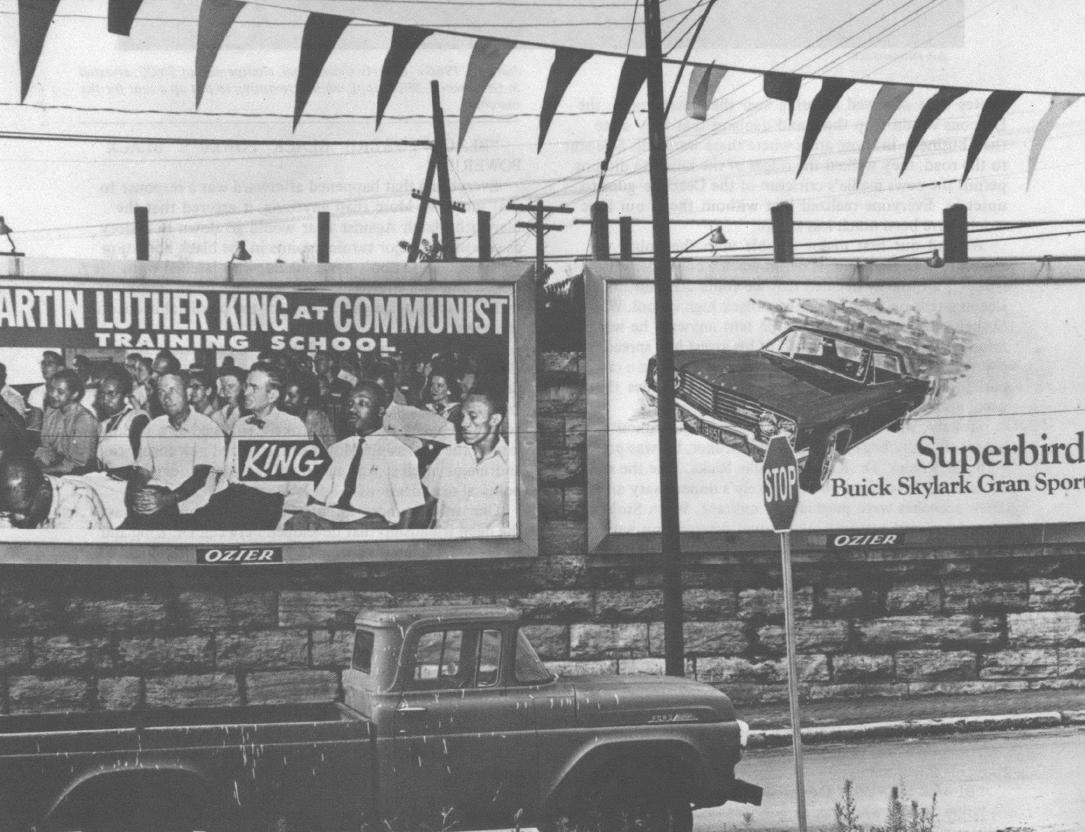 Black and white photo of truck parked in front of billboard that reads "Martin Luther King at Communist Training School"