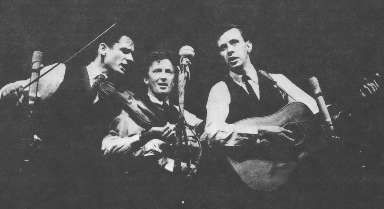 Black and white photo of three singing men around a microphone