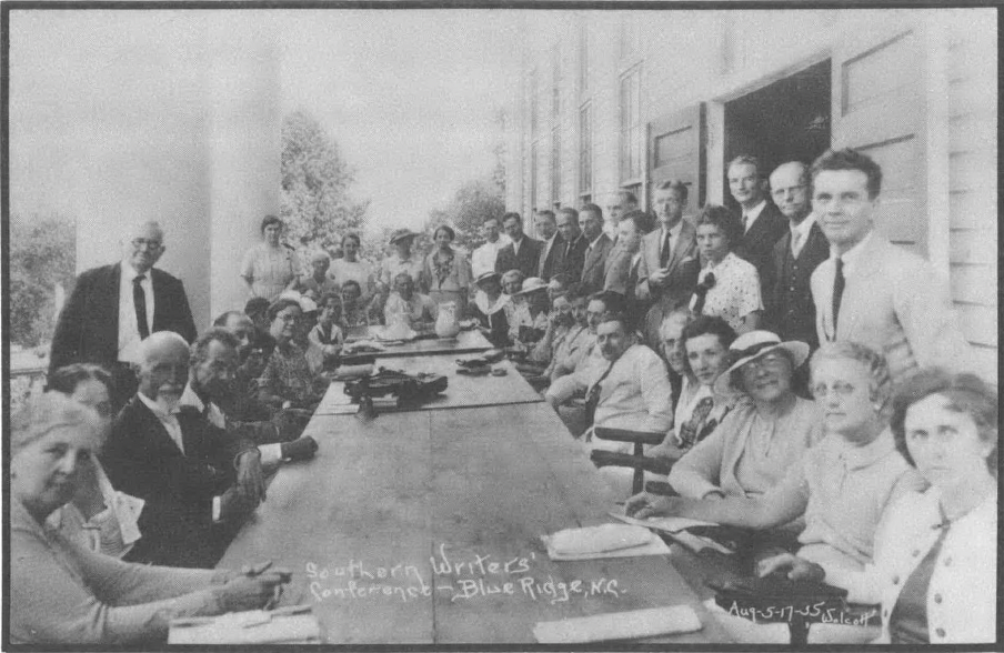 Black and white photo of a couple dozen people gathered around a table, facing the camera