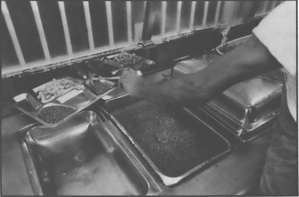 Black and white photo showing prison food with a man's arm reaching into the frame
