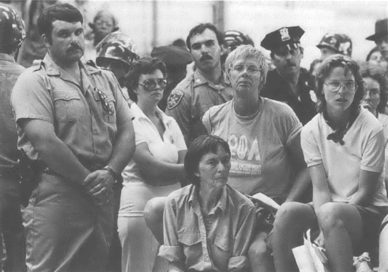 Picture of woman seated surrounded by people with hands clasped 