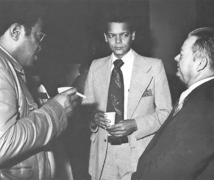 Black and white photo of three men in suits talking with each other, one of them Julian Bond