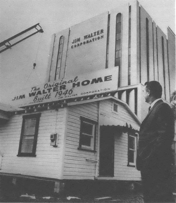 Black and white photo of man standing in front of sign on building reading "Jim Walter Homes"