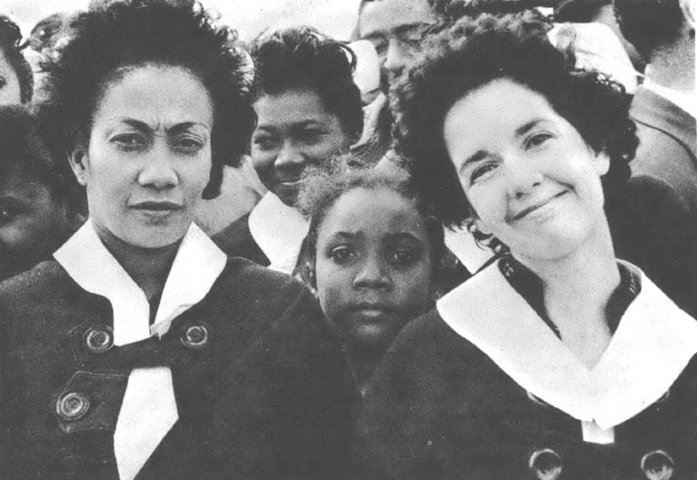 Three Black women and a Black girl, of varying skin tones, wearing uniforms and looking at the camera