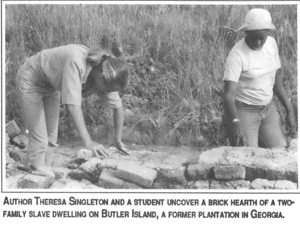 two people in a field, kneeling on dirt with text "AUTHOR THERESA SINGLETON AND A STUDENT UNCOVER A BRICK HEARTH OF A TWO FAMILY SLAVE DWELLING ON BUTLER ISLAND, A FORMER PLANTATION IN GEORGIA."