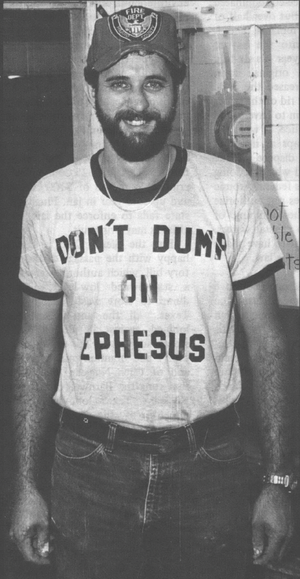 Black and white photo of young white man in baseball cap and shirt reading "Don't Dump on Ephesus"