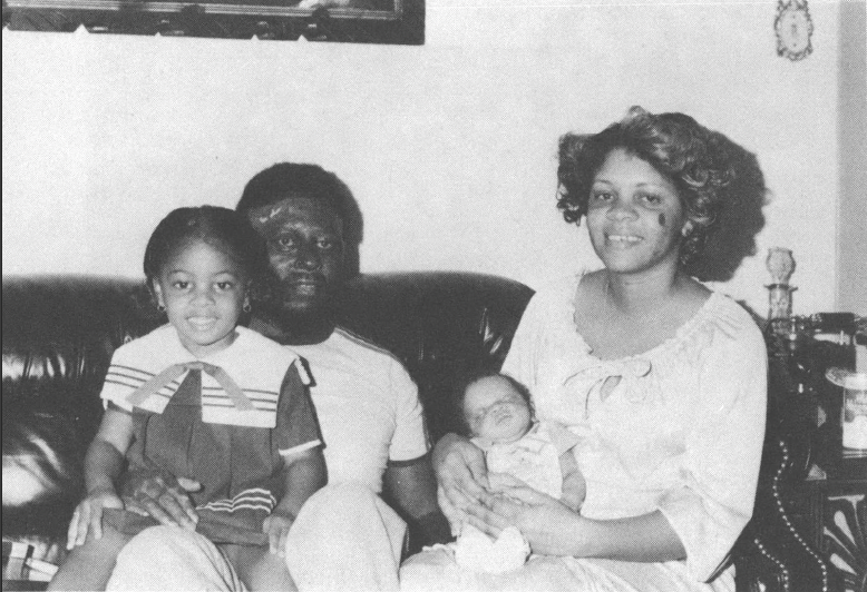 Black and white photo of Black family seated on couch smiling at camera