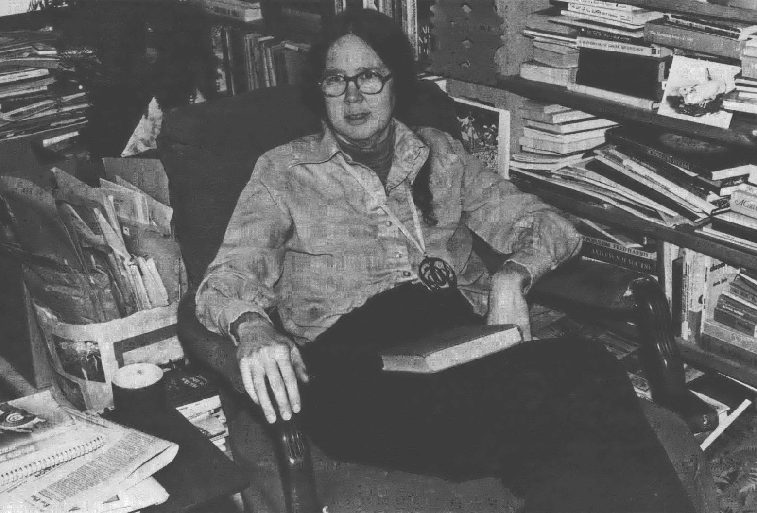 Black and white photo of white woman reclining in chair surrounded by books